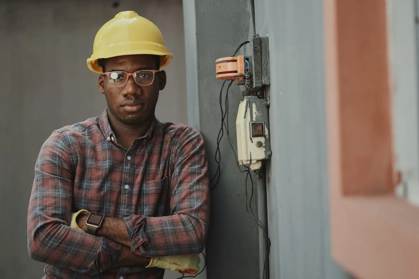 Electrician in a hard hat standing beside a wall installation